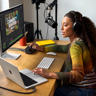 Eine Frau arbeitet an ihrem Schreibtisch zu Hause mit einem MacBook Pro, das mit zwei externen Displays verbunden ist. Sie trägt Kopfhörer und spricht in ein Mikrofon